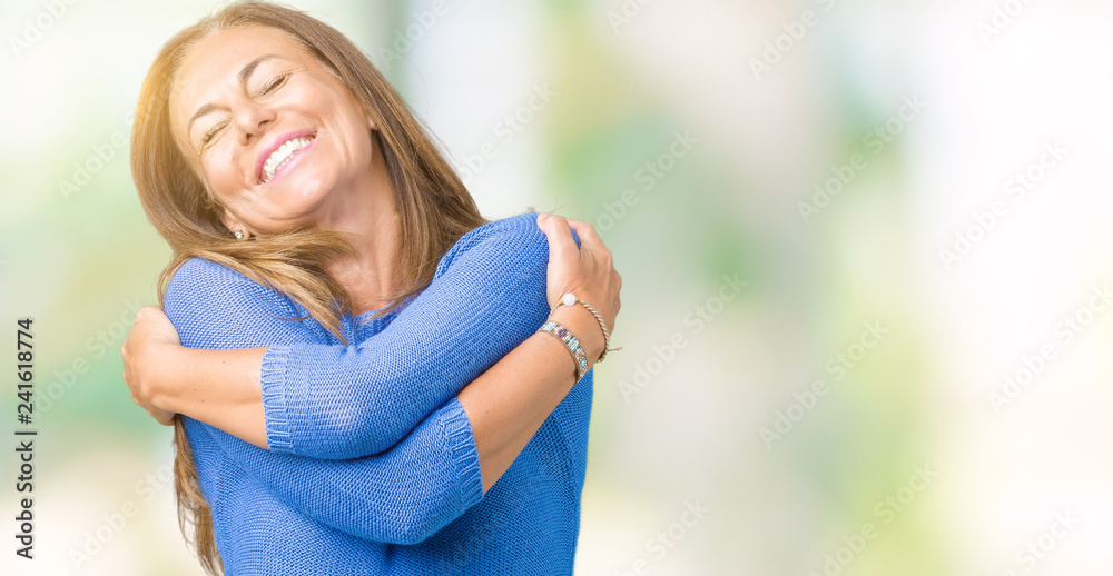 Fototapeta premium Średnim wieku piękna kobieta ubrana w zimowy sweter na pojedyncze tle Przytulanie się szczęśliwy i pozytywny, uśmiechając się pewnie. Self love i self care