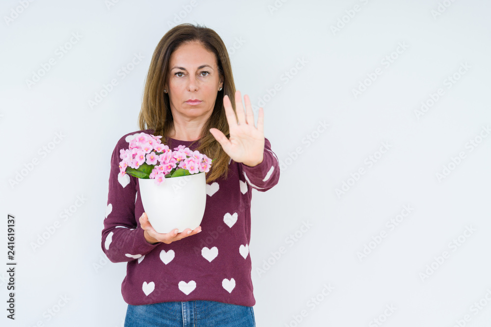 Middle age woman holding flowers pot plant over isolated background with open hand doing stop sign with serious and confident expression, defense gesture Middle age woman holding flowers pot plant over isolated background with open hand doing stop sign with serious and confident expression, defense gesture