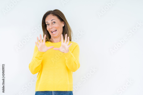 Beautiful middle age woman wearing yellow sweater over isolated background afraid and terrified with fear expression stop gesture with hands, shouting in shock. Panic concept.