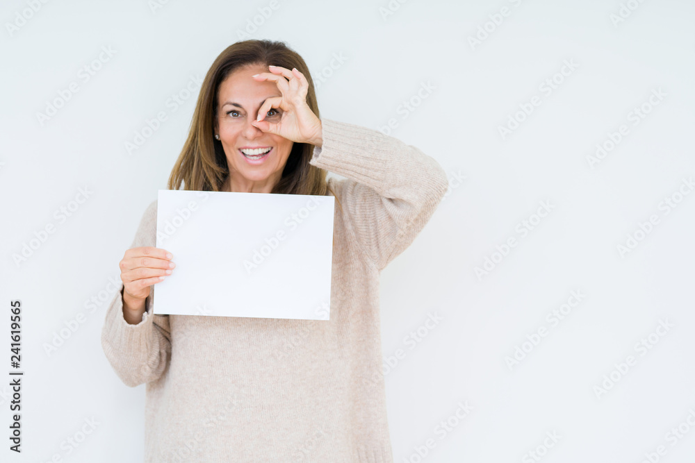 Middle age woman holding blank paper sheet over isolated background with happy face smiling doing ok sign with hand on eye looking through fingers Middle age woman holding blank paper sheet over isolated background with happy face smiling doing ok sign with hand on eye looking through fingers