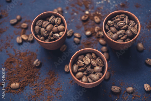 Coffee beans in ceramic cups and ground coffee on a dark background. Top view.