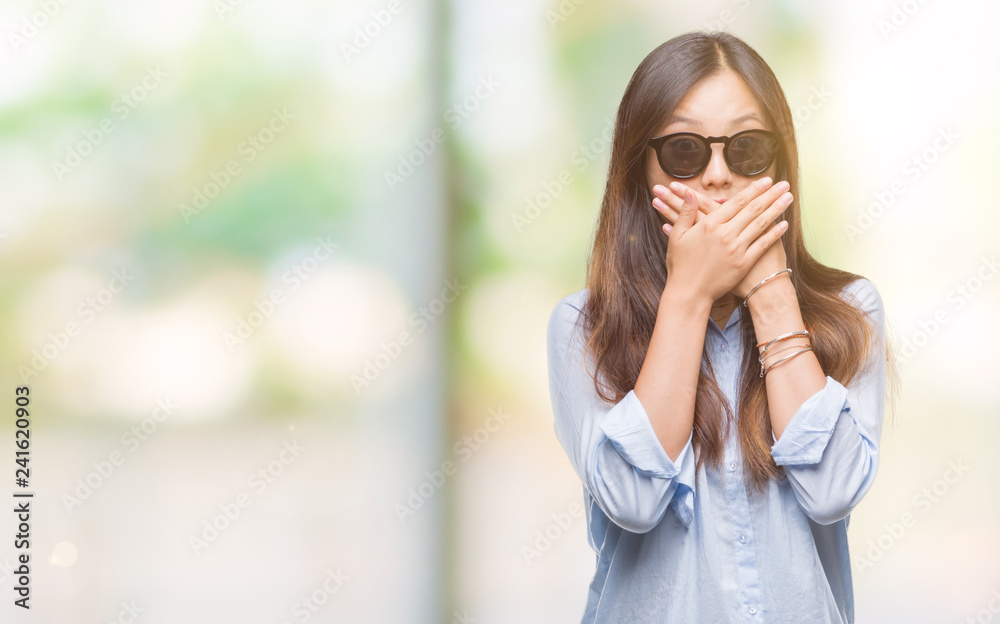 Fototapeta premium Young asian woman wearing sunglasses over isolated background shocked covering mouth with hands for mistake. Secret concept.
