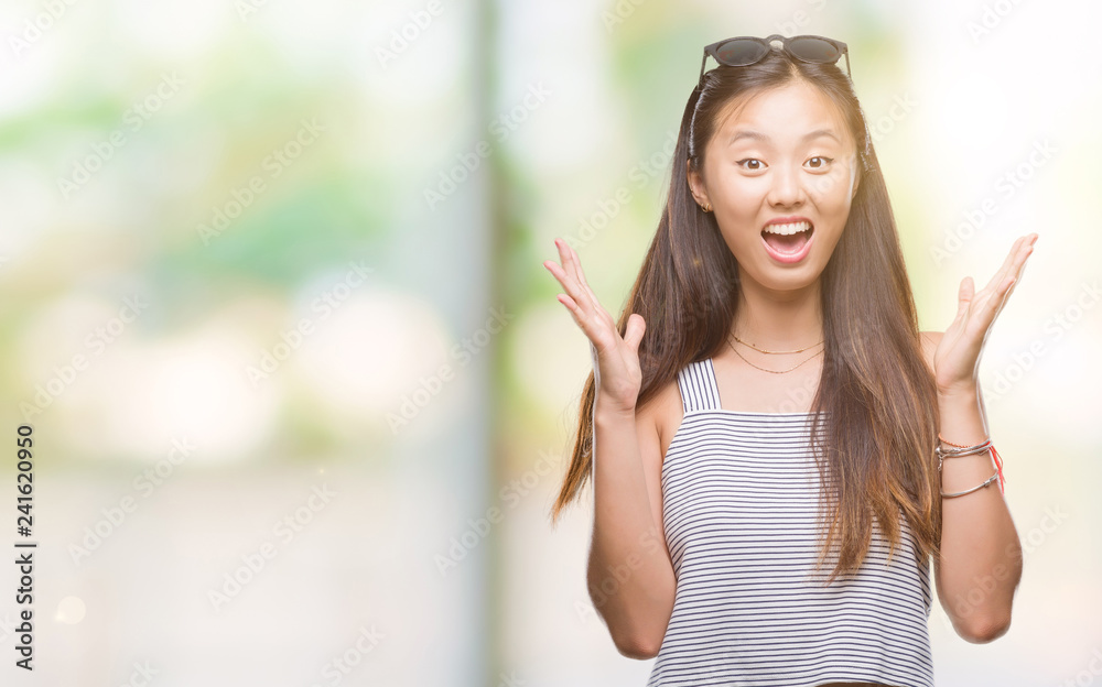 Young asian woman wearing sunglasses over isolated background celebrating crazy and amazed for success with arms raised and open eyes screaming excited. Winner concept Young asian woman wearing sunglasses over isolated background celebrating crazy and amazed for success with arms raised and open eyes screaming excited. Winner concept