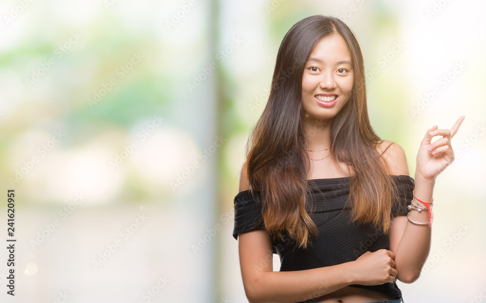 Young asian woman over isolated background with a big smile on face, pointing with hand and finger to the side looking at the camera.