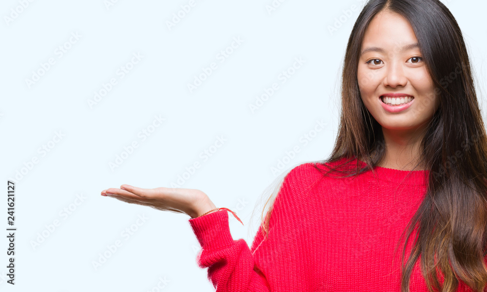 Young asian woman wearing winter sweater over isolated background smiling cheerful presenting and pointing with palm of hand looking at the camera. Young asian woman wearing winter sweater over isolated background smiling cheerful presenting and pointing with palm of hand looking at the camera.