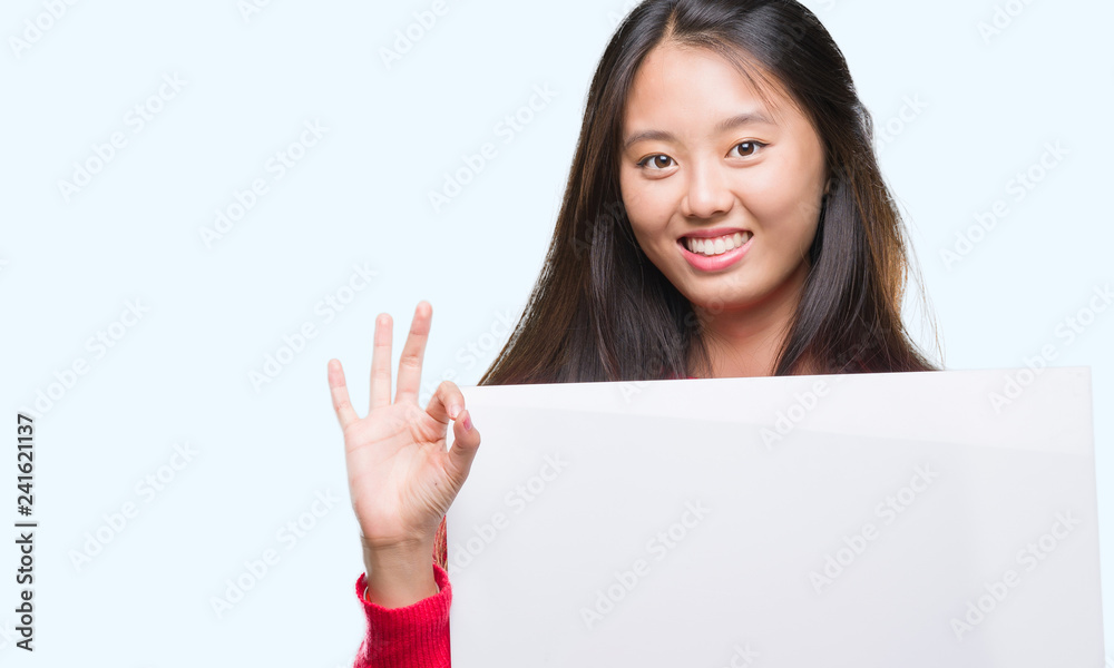 Young asian woman holding banner over isolated background doing ok sign with fingers, excellent symbol Young asian woman holding banner over isolated background doing ok sign with fingers, excellent symbol