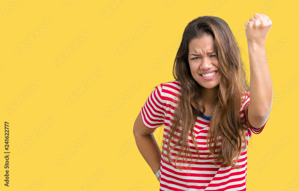 Young beautiful brunette woman wearing stripes t-shirt over isolated background angry and mad raising fist frustrated and furious while shouting with anger. Rage and aggressive concept.
