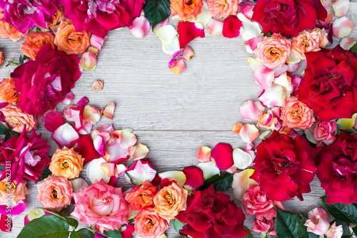 Frame heart made of rose flowers on wooden background for Valentines day. Flat lay, copy space