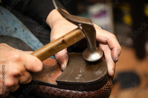 close-up of hands male shoemaker repairing shoes by nailing a heel photo