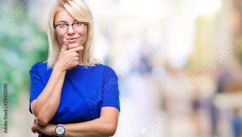 Young beautiful blonde woman wearing glasses over isolated background looking confident at the camera with smile with crossed arms and hand raised on chin. Thinking positive.