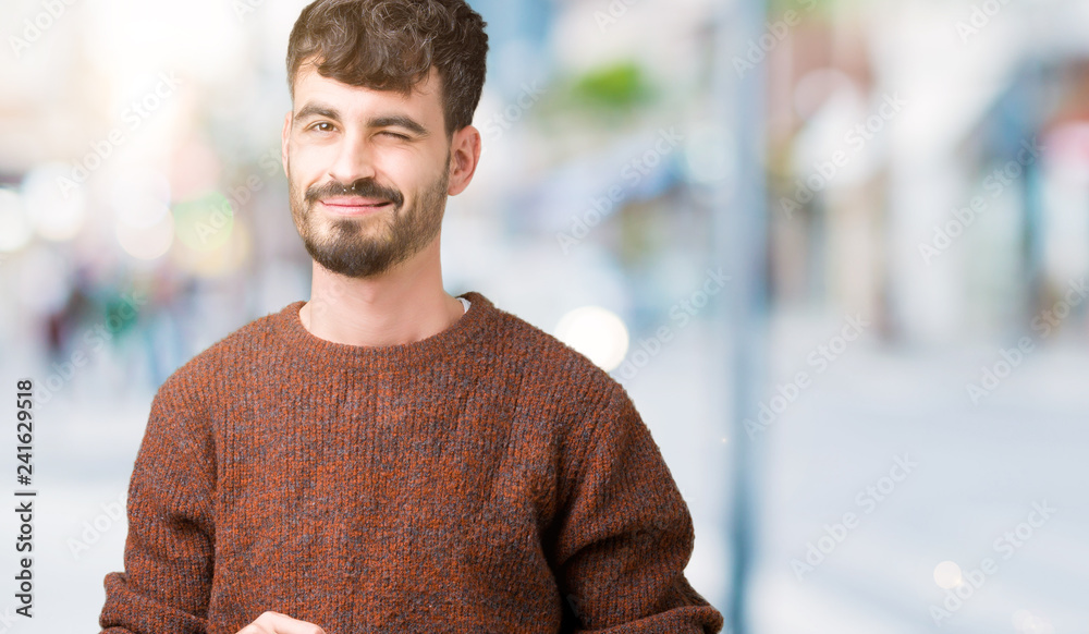 Fototapeta premium Young handsome man wearing winter sweater over isolated background winking looking at the camera with sexy expression, cheerful and happy face.
