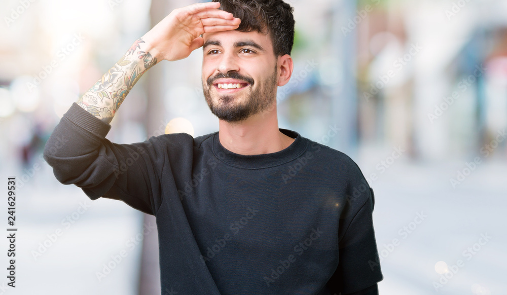 Fototapeta premium Young handsome man over isolated background very happy and smiling looking far away with hand over head. Searching concept.
