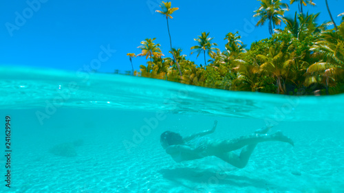 HALF HALF: Female tourist diving along the sandy beach in pristine ocean water