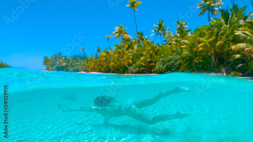 Fototapeta Naklejka Na Ścianę i Meble -  HALF UNDERWATER: Carefree girl on holiday swimming in the glassy ocean water.
