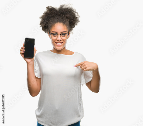 Young beautiful afro american showing smartphone screen over isolated background with surprise face pointing finger to himself