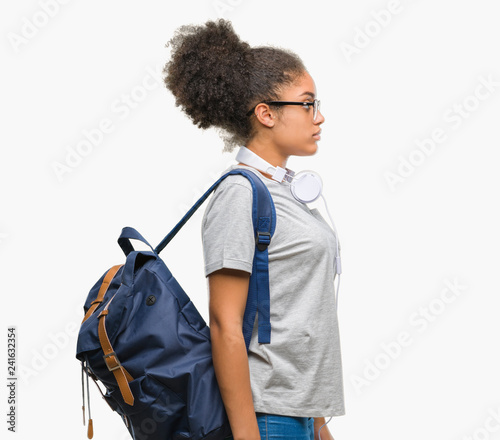 Young afro american student woman wearing headphones and backpack over isolated background looking to side, relax profile pose with natural face with confident smile.