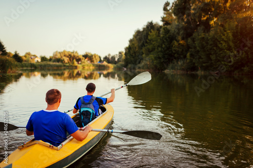 Young men rowing kayak on river at sunset. Couple of friends having fun canoeing in summer