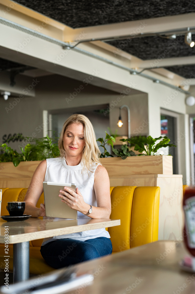 Confident woman with coffee on table using tablet computer while sitting in cafeteria