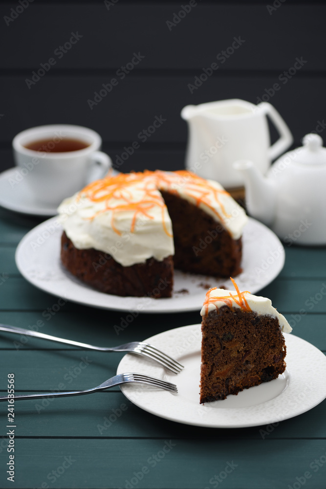 Chocolate fruit cake with cream cheese glasing and orange peel served with black tea on dark background Chocolate fruit cake with cream cheese glasing and orange peel served with black tea on dark background