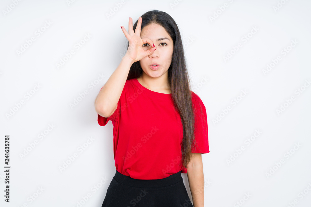 Beautiful brunette woman wearing red t-shirt over isolated background doing ok gesture shocked with surprised face, eye looking through fingers. Unbelieving expression. Beautiful brunette woman wearing red t-shirt over isolated background doing ok gesture shocked with surprised face, eye looking through fingers. Unbelieving expression.