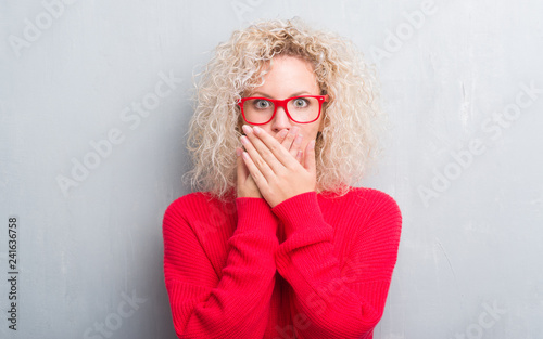 Young blonde woman with curly hair over grunge grey background shocked covering mouth with hands for mistake. Secret concept.