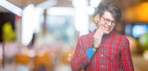 Young handsome man wearing glasses over isolated background touching mouth with hand with painful expression because of toothache or dental illness on teeth. Dentist concept.