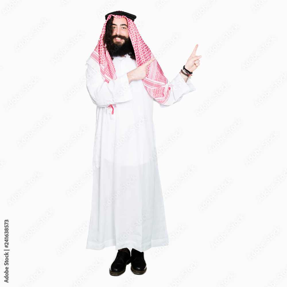 Arabian business man with long hair wearing traditional keffiyeh scarf smiling and looking at the camera pointing with two hands and fingers to the side. Arabian business man with long hair wearing traditional keffiyeh scarf smiling and looking at the camera pointing with two hands and fingers to the side.
