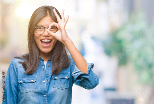 Young asian woman wearing glasses over isolated background doing ok gesture with hand smiling, eye looking through fingers with happy face.