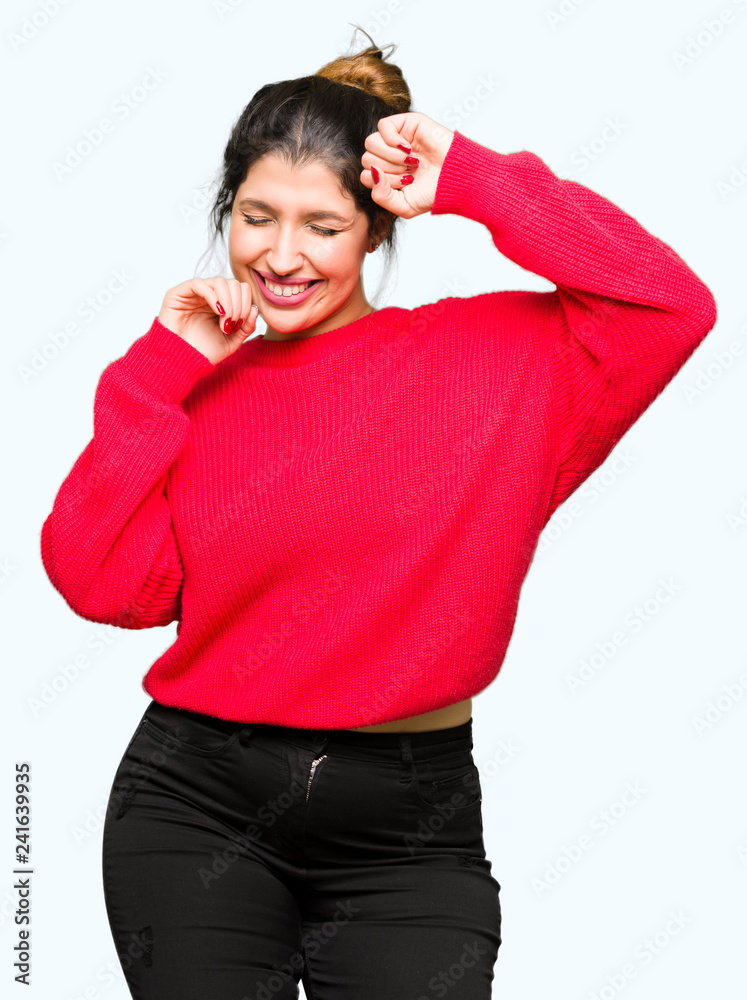 Young beautiful woman wearing red sweater and bun very happy and excited doing winner gesture with arms raised, smiling and screaming for success. Celebration concept. Young beautiful woman wearing red sweater and bun very happy and excited doing winner gesture with arms raised, smiling and screaming for success. Celebration concept.