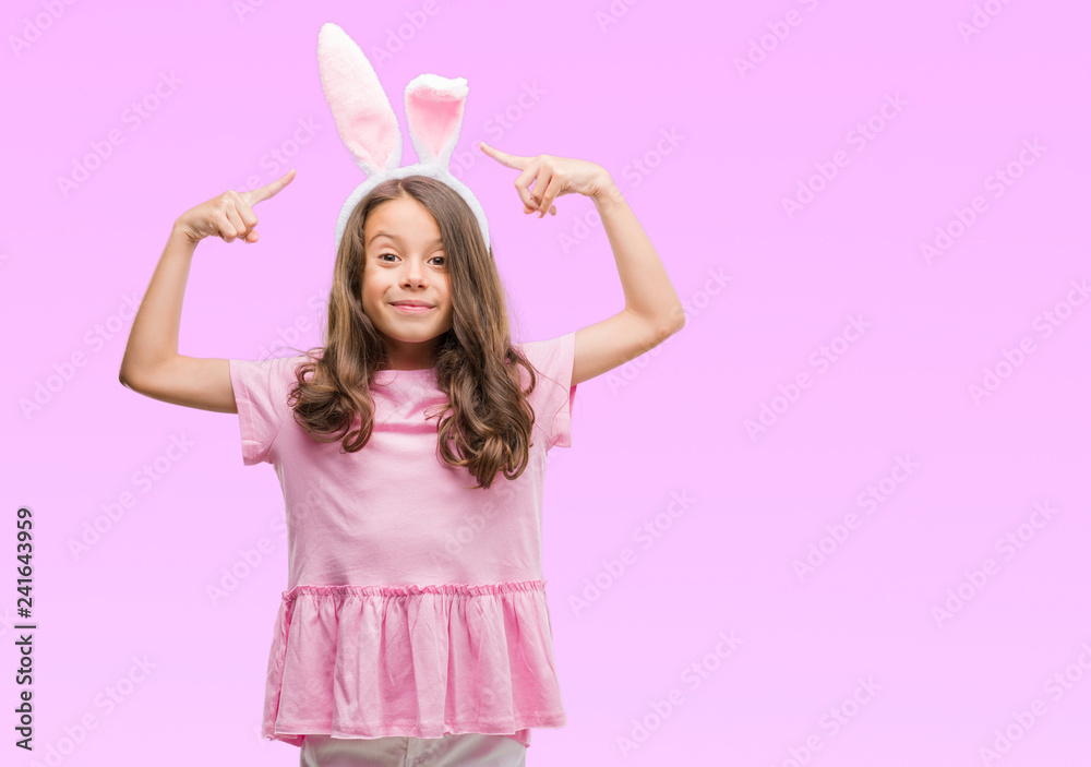 Brunette hispanic girl wearing easter rabbit ears very happy pointing with hand and finger Brunette hispanic girl wearing easter rabbit ears very happy pointing with hand and finger