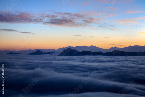 Canvas Print Sunset, Mountains and The Sea of Clouds - Snow Mountains in the distance protruding above a blanket of clouds like islands in an ocean - vibrant sunset sky, peaceful tranquility