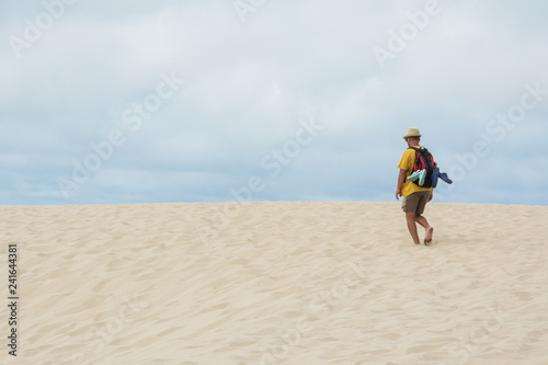 young man with backpack going in the sandy desert