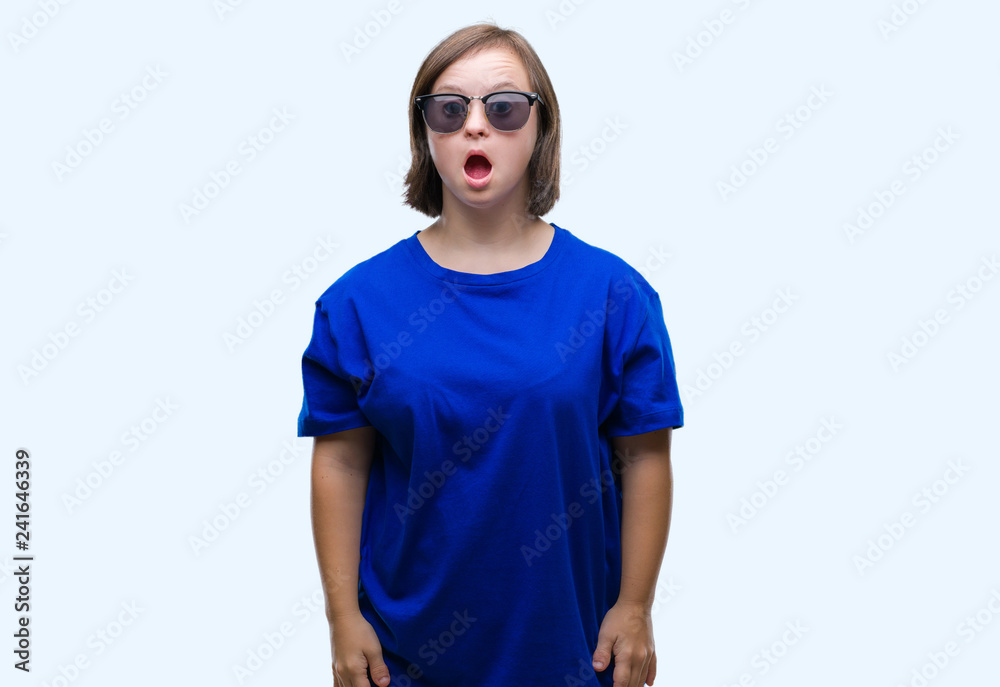 Young adult woman with down syndrome wearing sunglasses over isolated background afraid and shocked with surprise expression, fear and excited face.