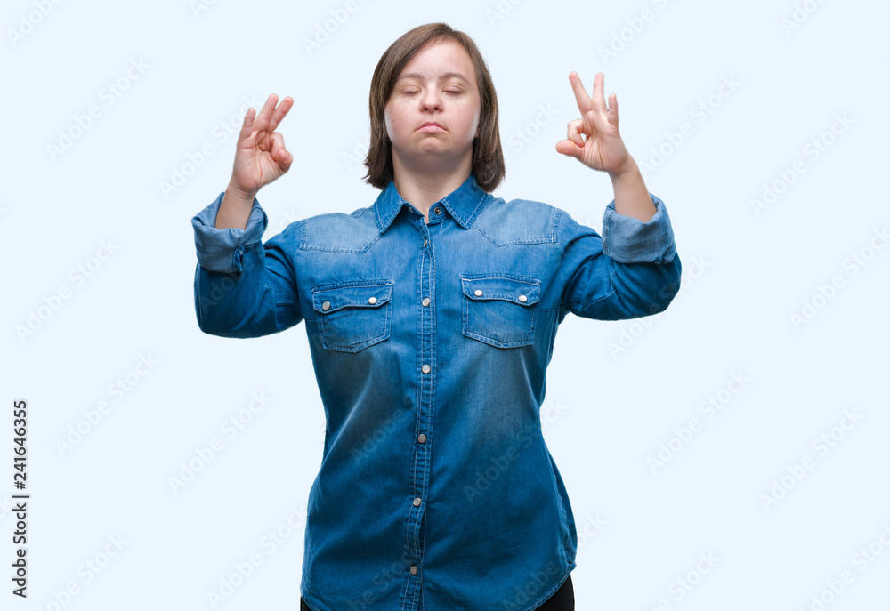 Young adult woman with down syndrome over isolated background relax and smiling with eyes closed doing meditation gesture with fingers. Yoga concept. Young adult woman with down syndrome over isolated background relax and smiling with eyes closed doing meditation gesture with fingers. Yoga concept.