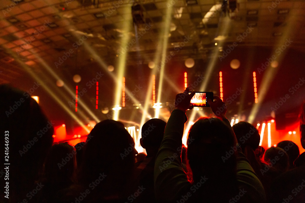 Silhouettes of crowds of spectators at a concert with smartphones in their hands.