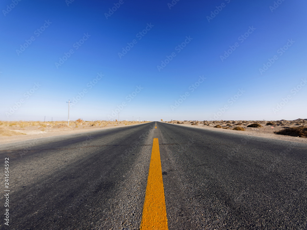 Centered view of an endless asphalt road in desert, low angle straight rough road with blue sky background, magic world.