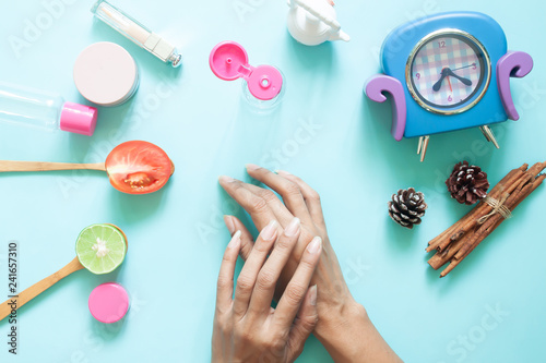 Woman's hands applying lotion on skin. Cosmetic containers and natural ingredient on pastel background
