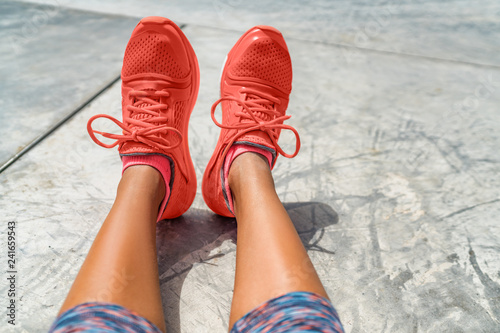 Running shoes woman fashion clothing in Pantone color of the year 2019 coral orange. Sporstwear sneakers for fitness clothes for women. POV selfie of feet on concrete floor at gym.