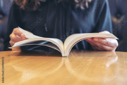 Closeup image of a woman holding and reading a book on wooden table