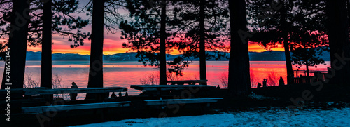 People enjoying an amazing sunset on the shoreline of Lake Tahoe; pine trees silhouettes in the foreground, California