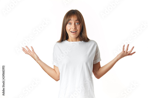 Unsure or doubting caucasian woman in white t-shirt throws up her arms in perplexity, without knowing how she managed to lose weight so quickly, isolated over white background