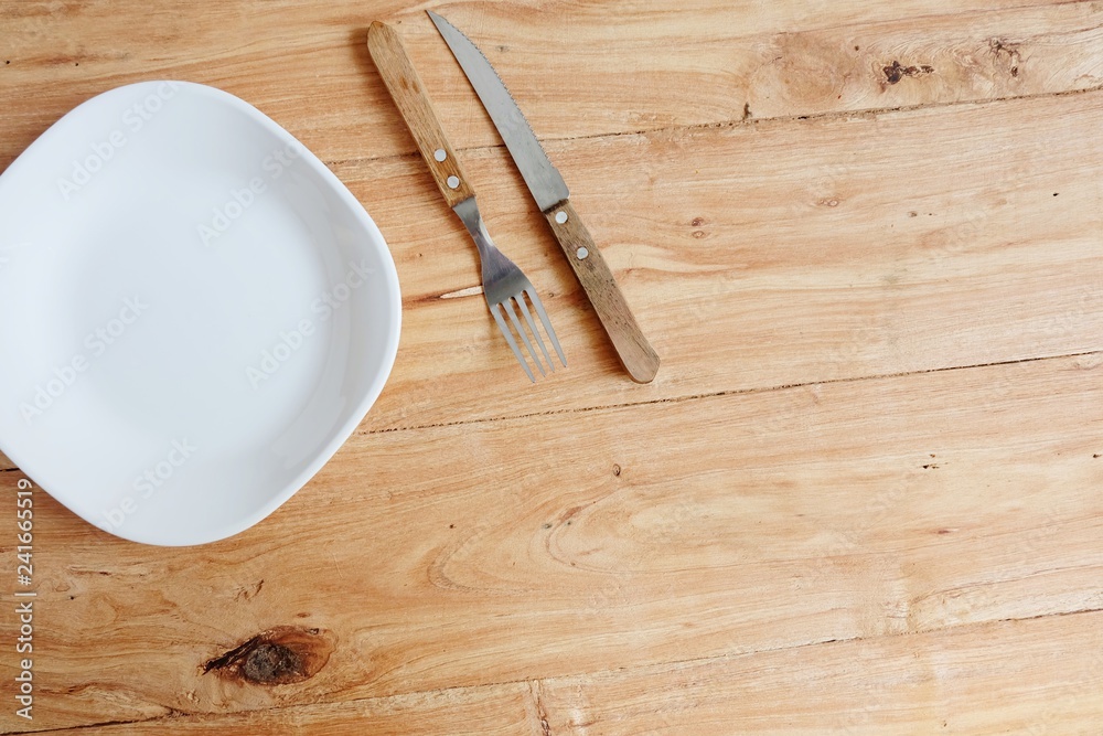 White plate with a fork and spoon On the wood background. Tableware. - Copy Space.