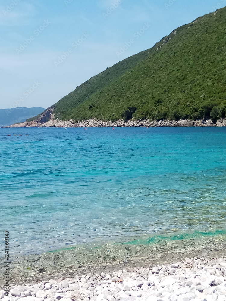 Rocky beach on the Adriatic Sea. Sunny summer day, windless weather. Blue ocean.