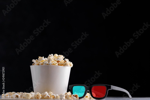 White paper cup with popcorn and glasses on a close background.