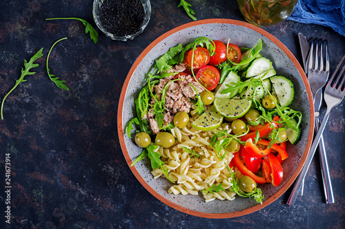 Buddha bowl. Pasta salad with tuna, tomatoes, olives, cucumber, sweet pepper and arugula on rustic background . Top view