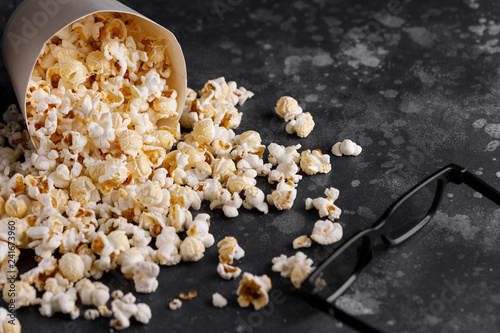 Snack for watching movies. Popcorn fallen out of a paper bucket on a textural background and glasses.