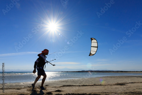 Professional kite boarding rider sportsman with kite in blue lagoon enjoying fun joy happy leisure rest relaxing time. Recreational activity, extreme active air water sports on sea. Man across sun