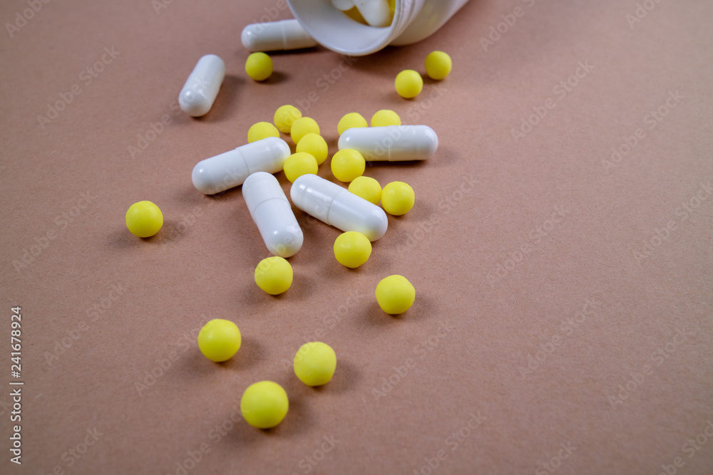Mixed pills spilled out of the white bottle. Pharmaceutical medicine tablets, capsules and pills on the brown background Mixed pills spilled out of the white bottle. Pharmaceutical medicine tablets, capsules and pills on the brown background