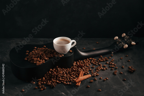 A cup of coffee is on a black ululele with scattered coffee beans, anise and cinnamon photo