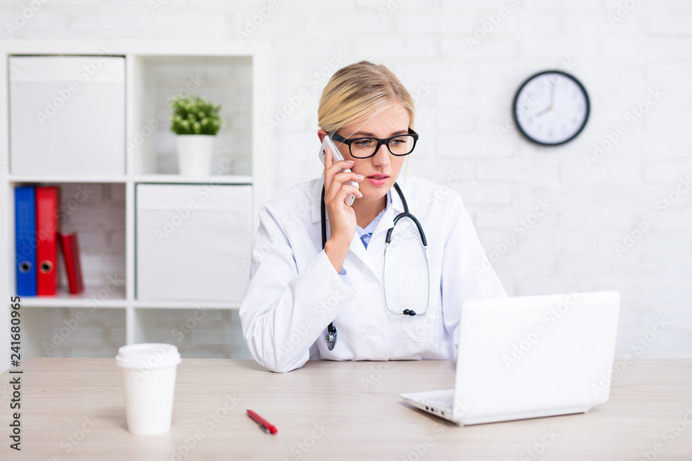 female doctor working with computer and talking by phone in office female doctor working with computer and talking by phone in office